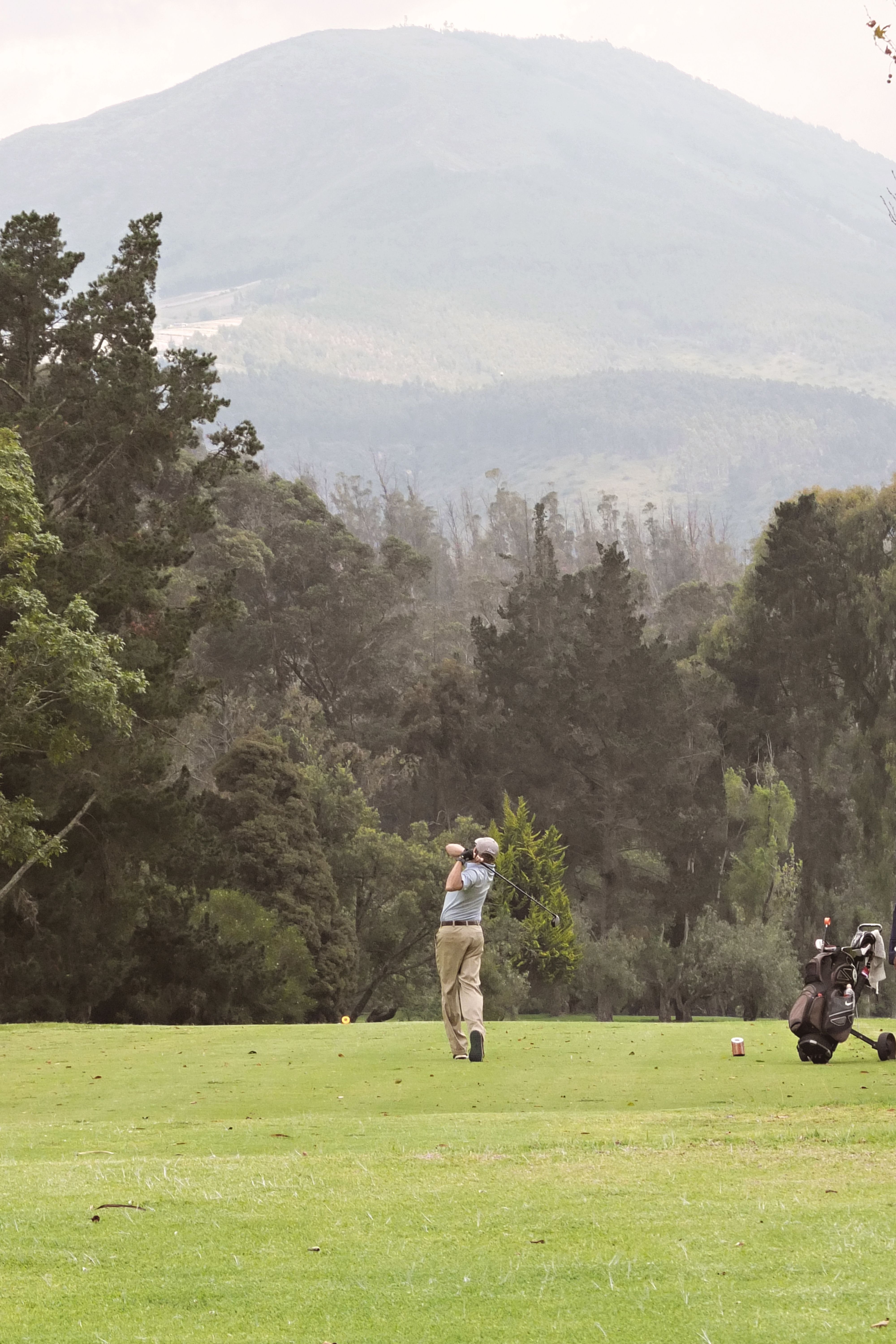 A golfer completing his swing on a scenic course with mountains and trees in the background